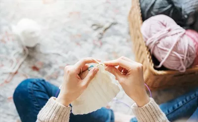 عکس زنی جوان در حال بافتن شال گرم در فضای داخلی منزل