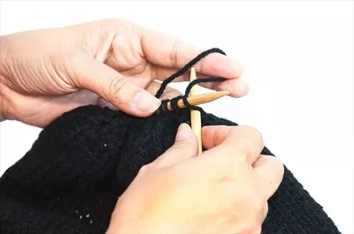 عکس زنی که در حال بافت کلاه مشکی با دستانش بر روی پس زمینه سفید است