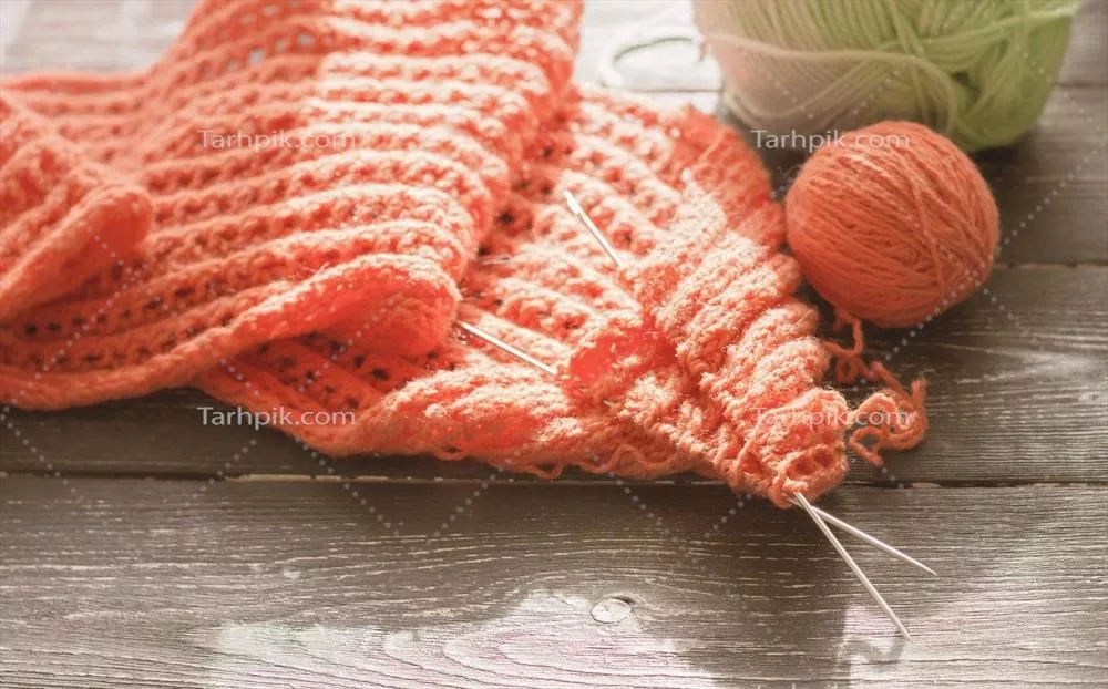 عکس تصویری از بافتنی با میل و کاموا نارنجی در حال تکمیل