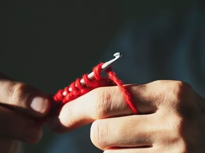 عکس نزدیک نمایی از قلاب بافی با نخ پشمی قرمز بر روی زمینه تیره