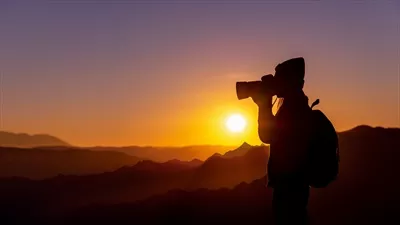 عکس عکاسی از یک زن جوان هیپی در غروب آفتاب بر فراز کوه با پس زمینه طبیعی