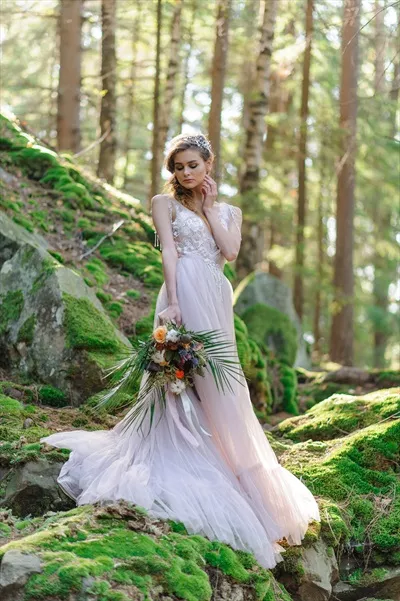 عکس عروس شاد در لباس عروسی صورتی با دسته گل در دست در مراسمی بوهو در جنگل