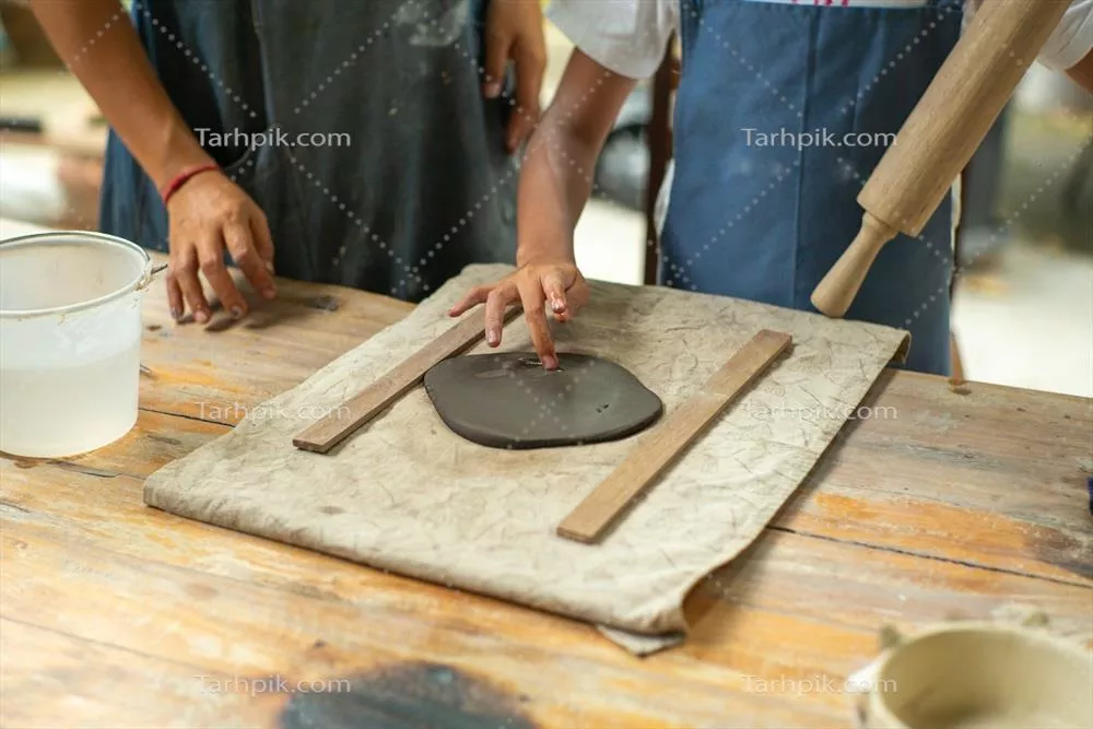 عکس نزدیک به دست های یک دختر در حال استفاده از وردنه بر روی گل در کارگاه سفالگری