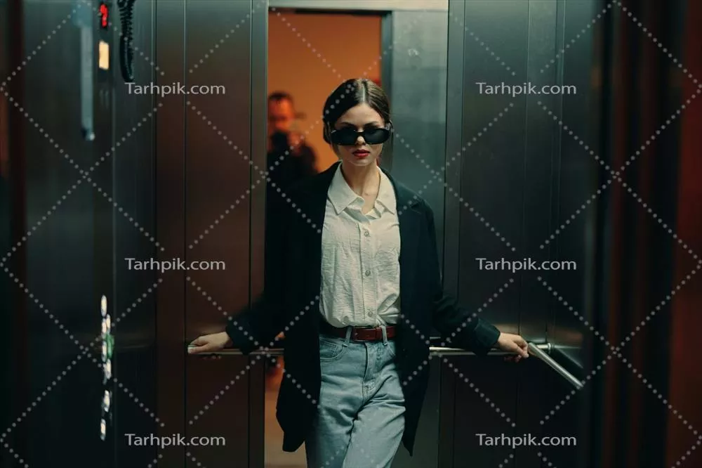 عکس زنی شیک در کت مشکی و عینک آفتابی در حال ژست گرفتن در آسانسور