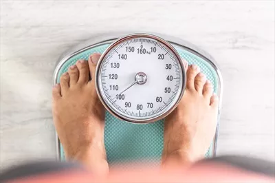 عکس زنی که در حال بررسی وزن خود بر روی ترازو ایستاده است