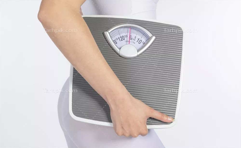 عکس مدل زن با ترازوی دستی و نوار اندازه گیری در پس زمینه سفید