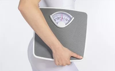 عکس مدل زن با ترازوی دستی و نوار اندازه گیری در پس زمینه سفید