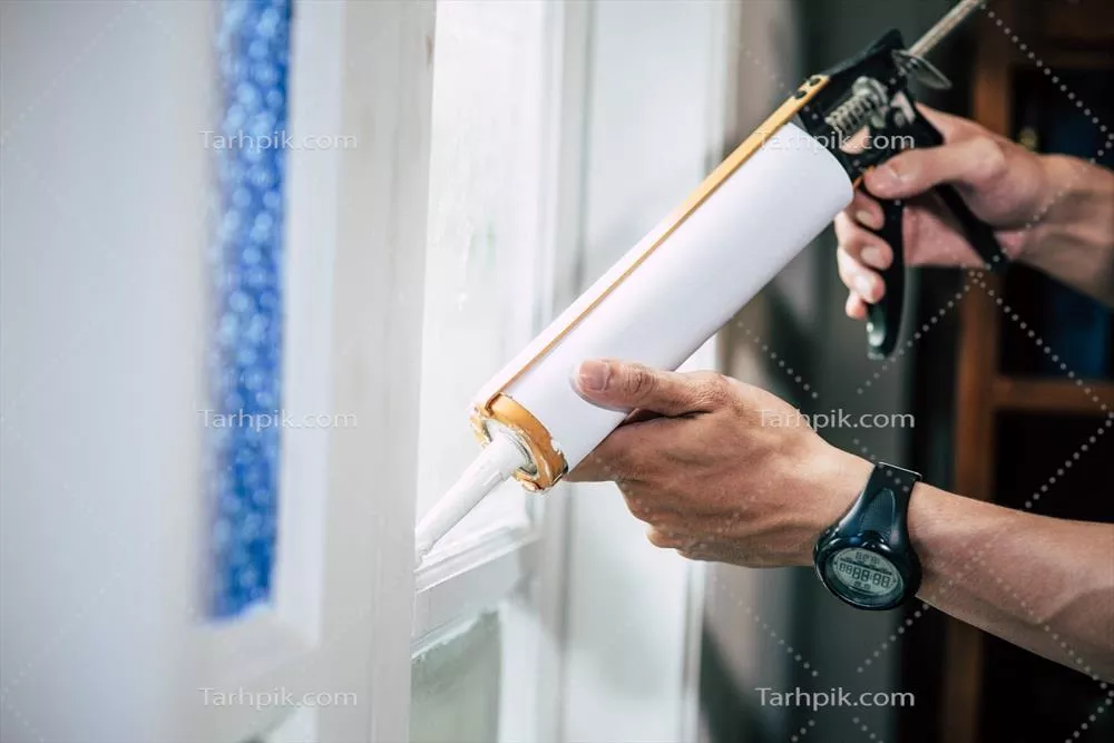 عکس نجار با دقت چسب را در دست دارد و پنجره را به آن متصل می کند