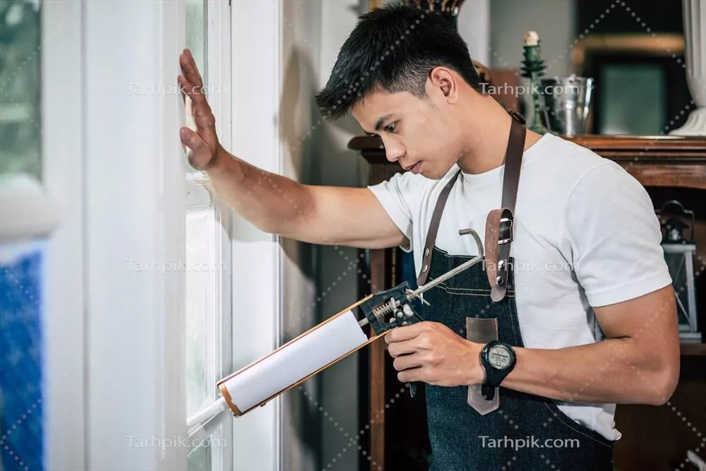 عکس نجار چسب را در دست دارد و آن را به پنجره متصل می کند