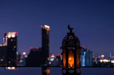 عکس چراغی با نماد ماه در بالای آن، در پس زمینه شب شهر برای جشن رمضان
