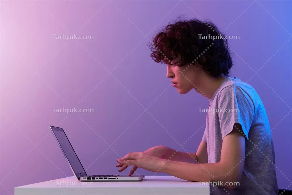 عکس مردی در دنیای سایبری در حال بازی با لپ تاپ در پس زمینه بنفش