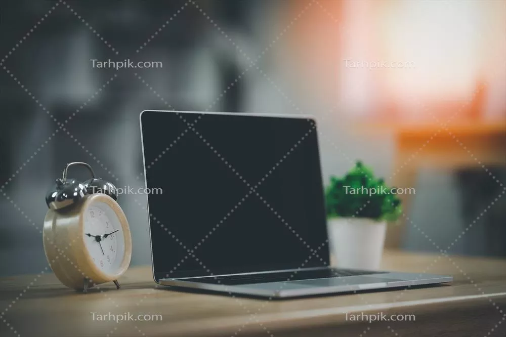 عکس فضای کاری مدرن با لپ تاپ و ساعت روی میز در یک محیط مشترک