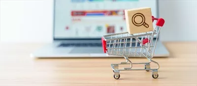 عکس تصویری از سبد خرید با آیکون ذره بین و لپ تاپ در حال نمایش وب سایت بازار آنلاین
