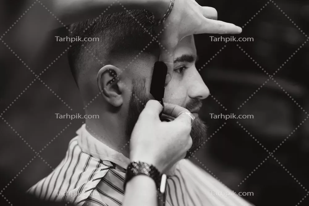 تصویر نزدیک از آرایشگری که با تیغ فولادی تیز مردی را اصلاح میکند