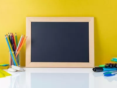 مفهوم بازگشت به مدرسه با تخته سیاه و وسایل مدرسه روی میز سفید در کنار دیوار زرد