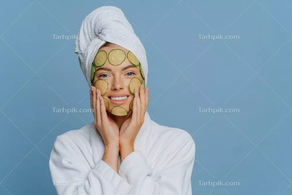 زن جوان و خوشحال که بر روی صورت خود برشهای خیار میگذارد و در حال انجام روشهای زیبایی است