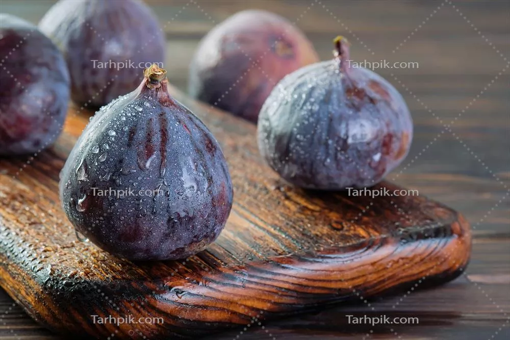 چندین انجیر رسیده با قطرات آب بر روی یک میز چوبی نزدیک به هم و تمرکز انتخابی بر میوههای فصلی و رژیم مدیترانهای