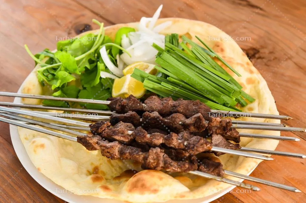 سرو کباب تیکا با نان تنوری بحرینی، لیمو و سالاد در بشقاب بر روی میز چوبی