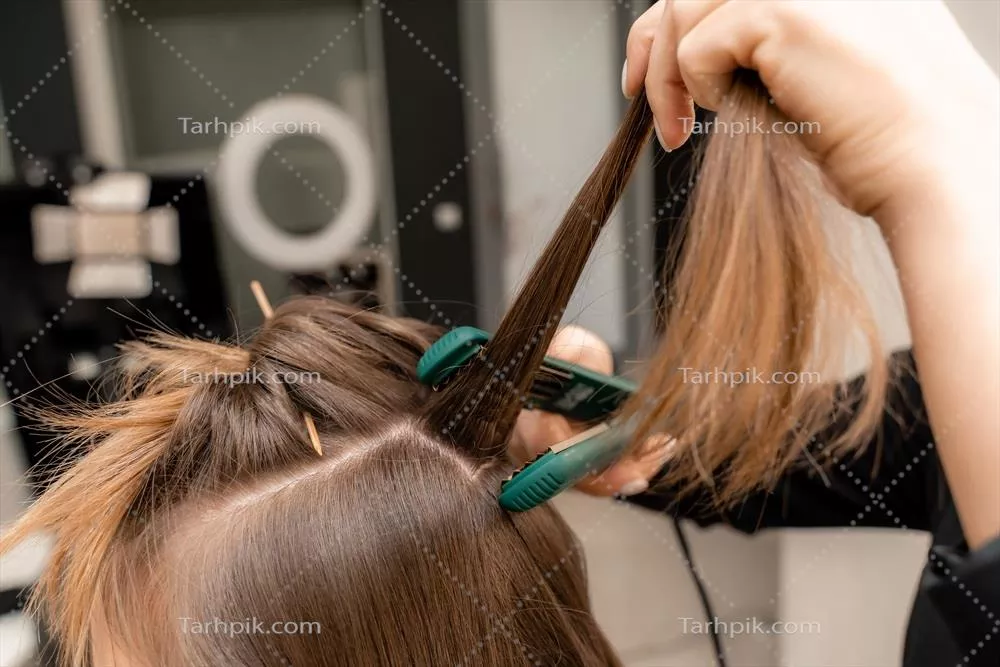 آرایشگر آماده‌سازی یک زن برای مدل مویی با فر به کمک صاف‌کننده مو
