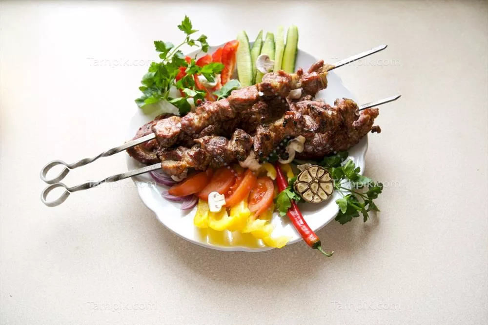 کباب‌های خانگی کبابی از گوشت خوک با سبزیجات روی بشقاب سنگی - نمای نزدیک افقی