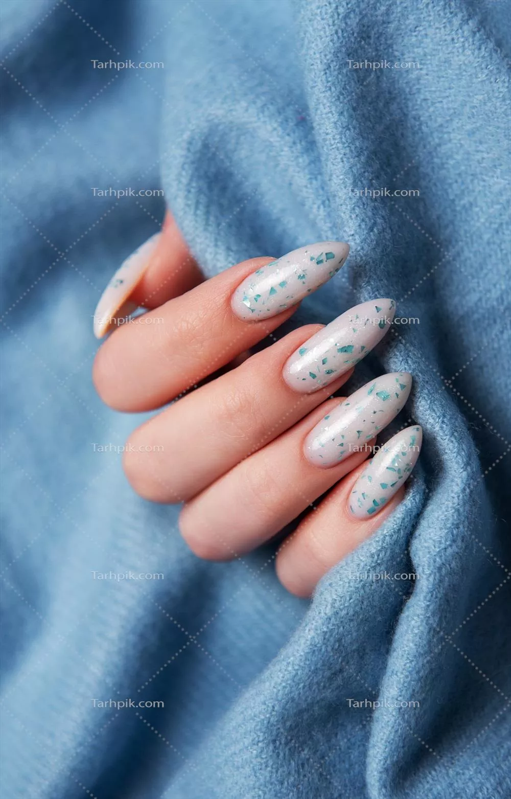 طراحی ناخن آبی بر روی دستان زنانه در پسزمینه پارچه ای آبی رنگ