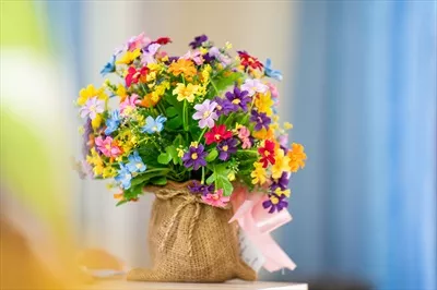 گلدان پلاستیکی با گل‌های مصنوعی در سبدی بافته شده روی میز در خانه