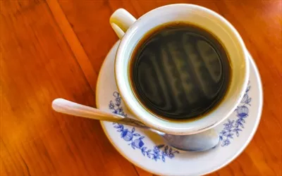فنجان آبی و سفیدی با قهوه سیاه بر روی یک میز چوبی در مکزیک