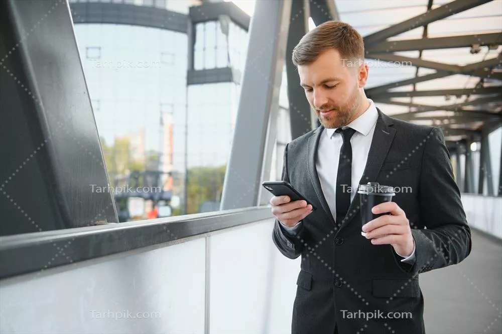 مرد کسب و کار ریشدار با کت و شلوار در خیابانهای مدرن شهری در حال استفاده از موبایل
