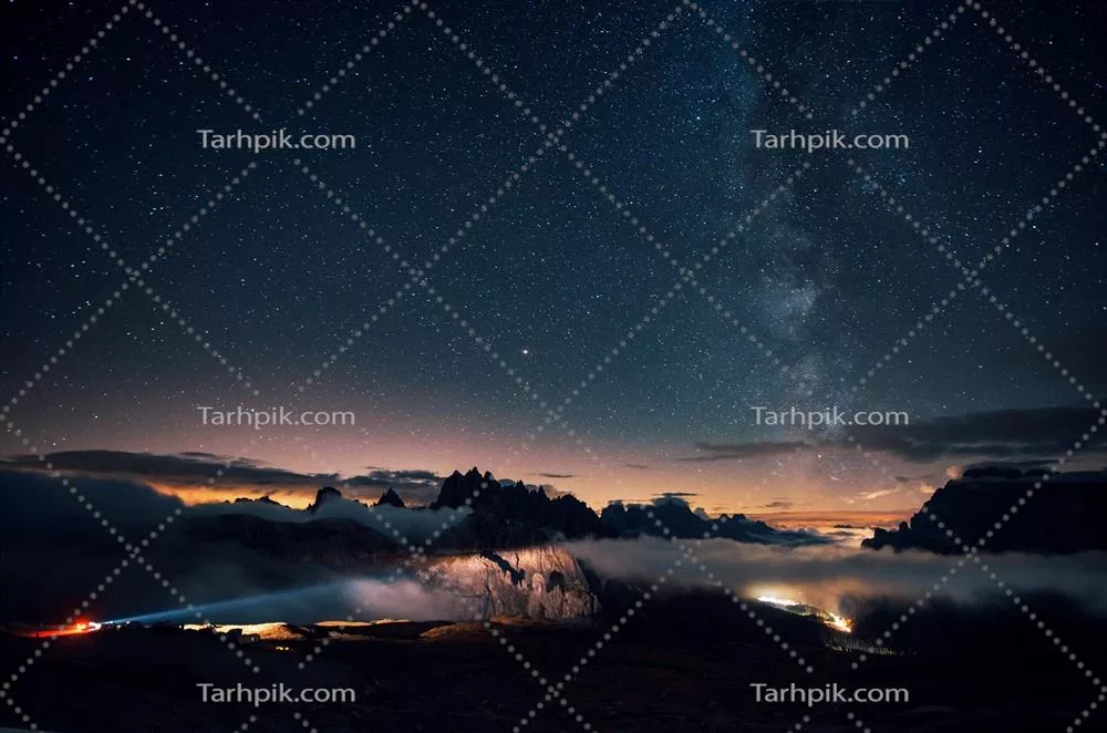 نورپردازی خودروهای دوردست در فضایی زیبا پر از ستارهها و مه غلیظ کوهها