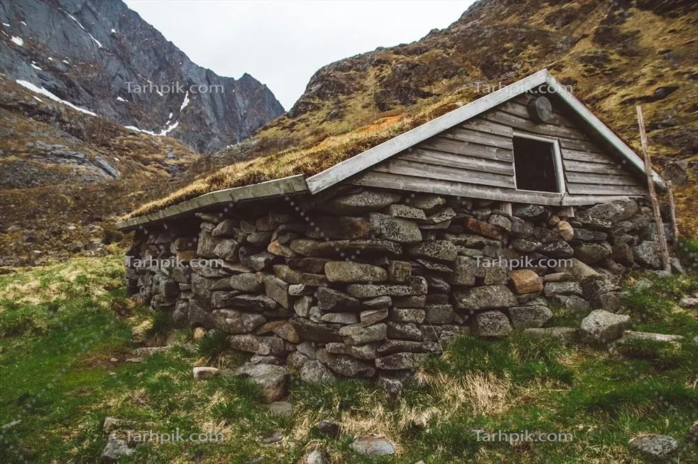 خانه‌ای قدیمی از سنگ و چوب پوشیده شده با خزه در پس‌زمینه کوه‌ها برای تبلیغات یا متن