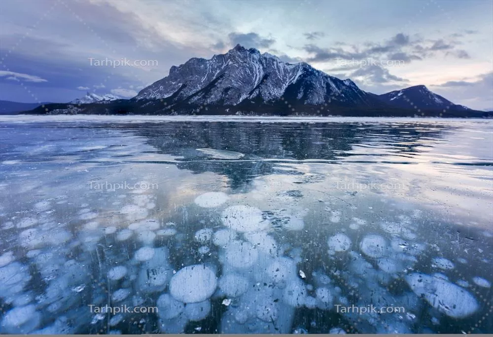 دریاچه منجمد آبرهام با کوه‌های سنگی و حباب‌های طبیعی در صبح زمستان در پارک ملی بانیف