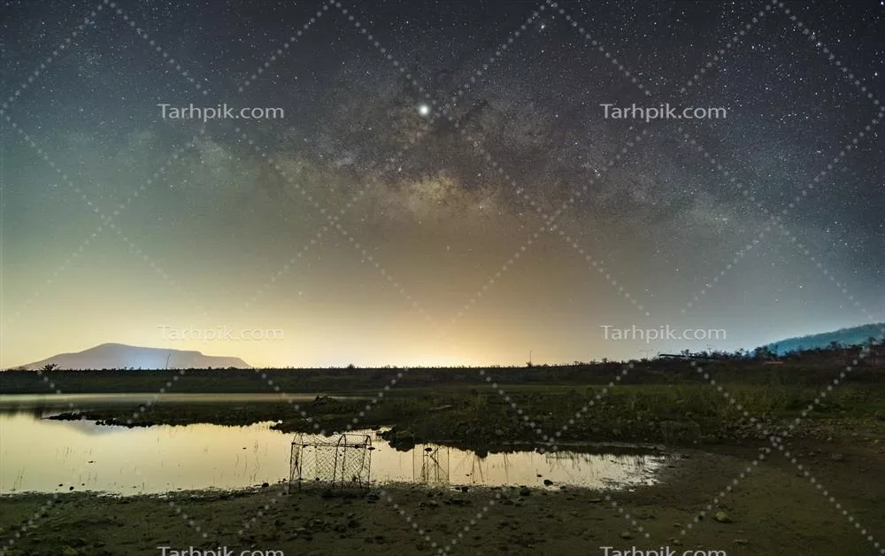 ستارگان در آسمان، نور شب را منعکس میکنند: کهکشان راه شیری در بالای کوهها و دریاچه سد و مخزن Mae Prachan در پچابوری تایلند