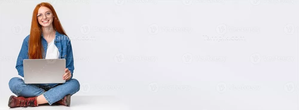 زنی جذاب با موهای قرمز و چهره ای شیک در حال کار با لپ تاپ روی زمین در فضای باز
