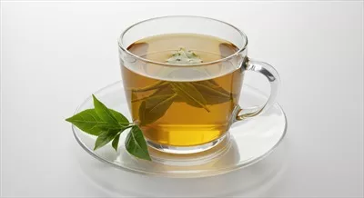 فنجان شیشهای چای گیاهی با برگهای سبز بر روی پسزمینه سفید
