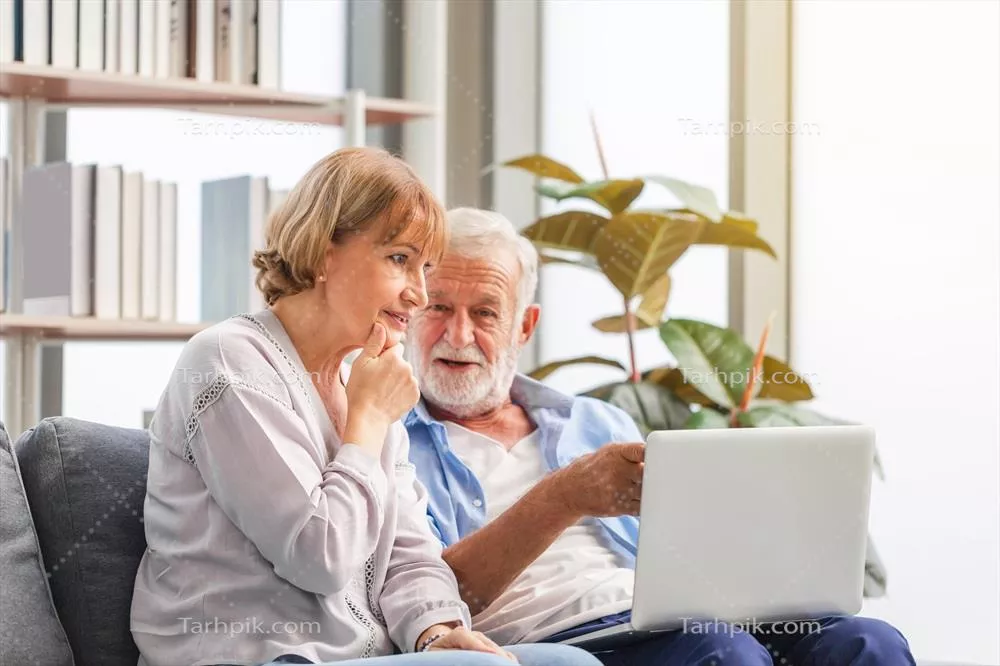 پرتره ای از یک زوج خوشحال سالخورده در اتاق نشیمن با استفاده از لپ تاپ