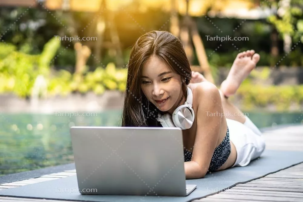 پرتره یک زن جوان آسیایی در حال کار با لپ‌تاپ در کنار استخر هتل