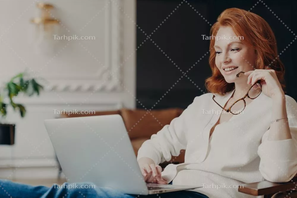 دانشجوی قرمزپوش و راضی در حال تماشای ویدیوهای آموزشی در خانه مدرن و دلباز