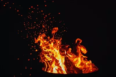 شعله‌های آتش کمپ در شب؛ آتش و جرقه‌ها در آسمان سیاه و فضایی برای متن