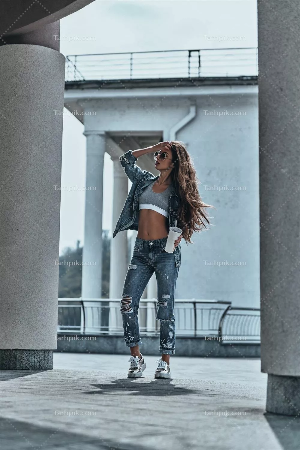 از همه چیز دور شو: مدل جوان جذاب در شلوار جین در حال قدم زدن با لیوان یکبار مصرف