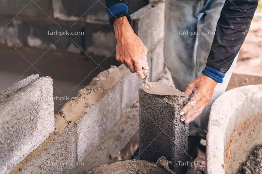 دست کارگر در حال گچ کاری و سیمان زنی بر روی دیوار آجری در محل ساخت و ساز