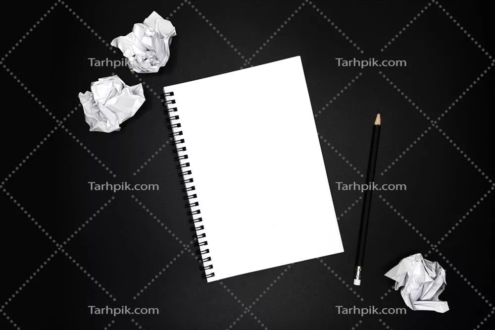 دفترچه یادداشت خالی با مداد مشکی و کاغذهای مچاله شده بر روی پس‌زمینه سیاه