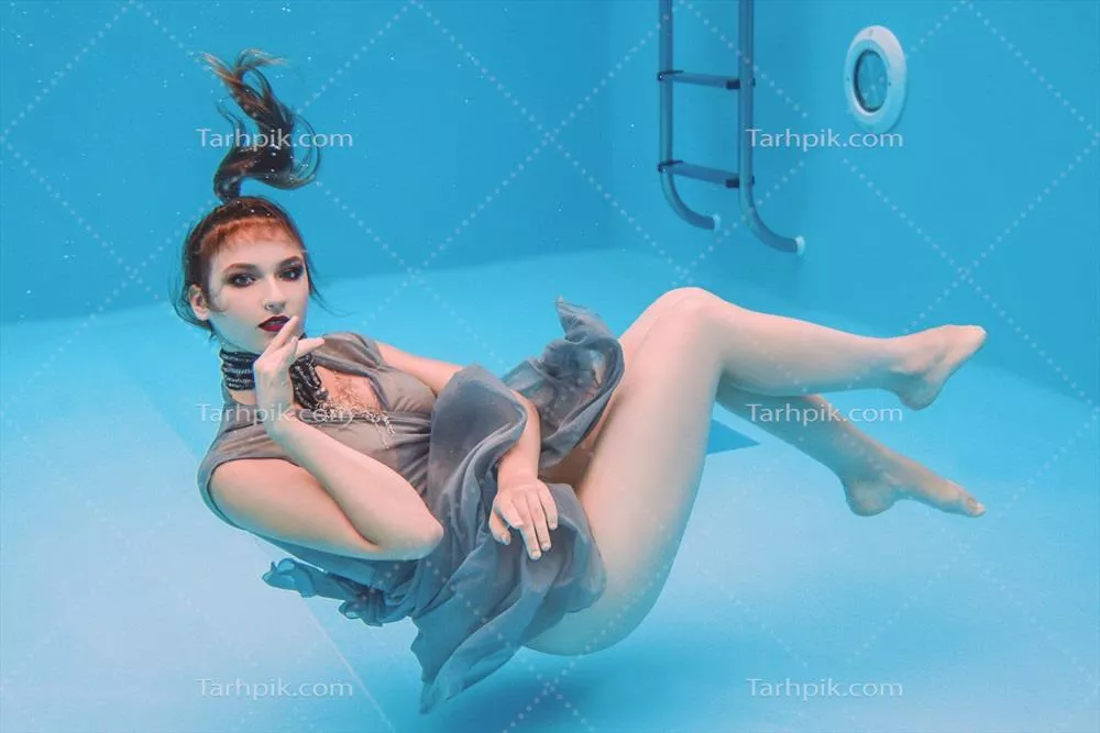 پرتره‌ای سوررئالیستی از زن جوان با لباس خاکستری و شال مرواریدی در زیر آب استخر