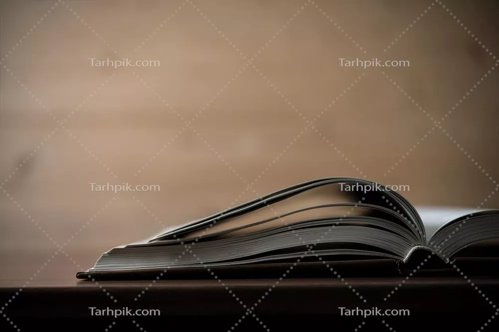 نمای نزدیک از یک کتاب باز شده بر روی میزی چوبی