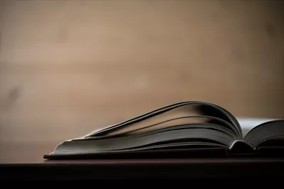 نمای نزدیک از یک کتاب باز شده بر روی میزی چوبی
