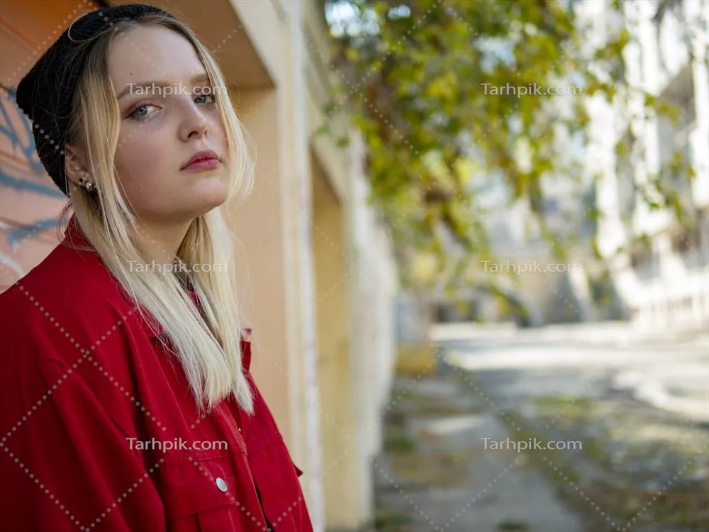 دختر زیبا با کلاه بافتنی و ژاکت قرمز در کنار دیوار ایستاده است