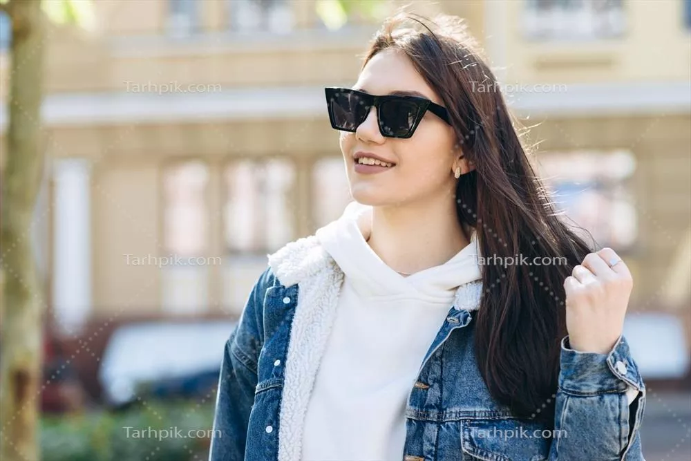 دختری جذاب با موهای تیره در حال پیادهروی در خیابان با لباس کژوال و عینک آفتابی