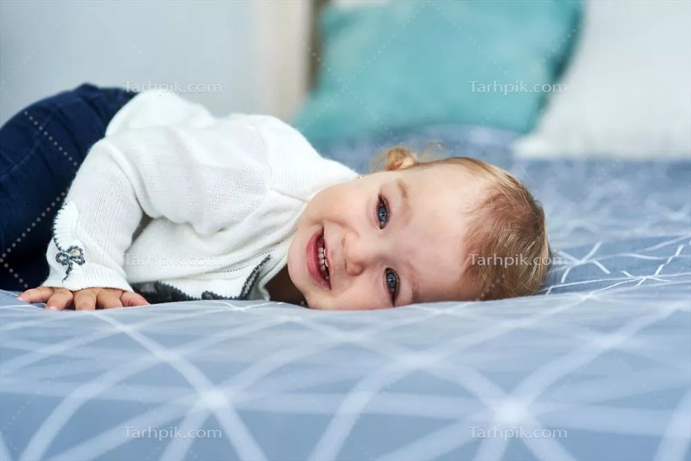 دختر بچه دوست داشتنی با لبخند در حال درازکشیدن روی تخت