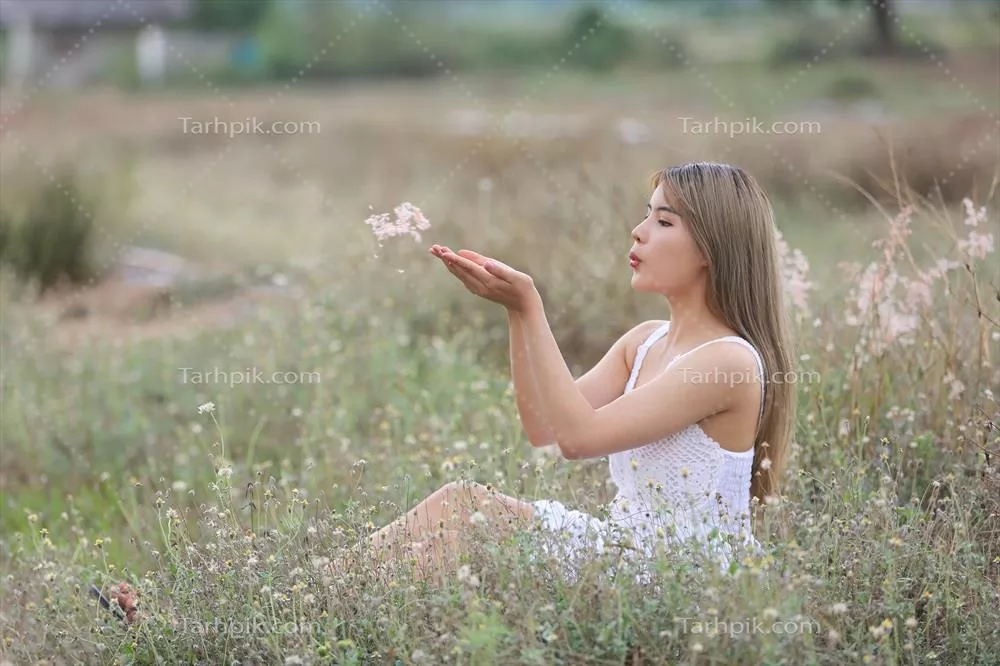 زنی جوان و زیبا در دل طبیعت، در حال دمیدن در دندکها بر چمن سبز