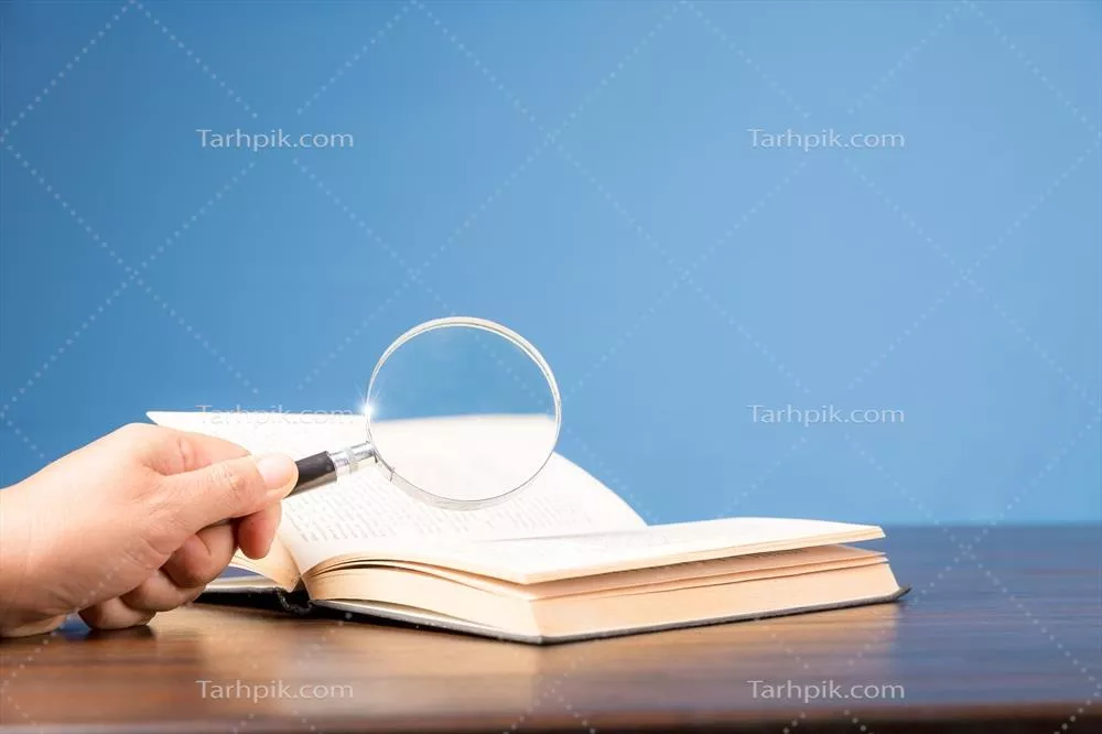 کتاب باز با ذره بین بر روی میز چوبی در کتابخانه اطلاعات مدرسه یا دانشگاه