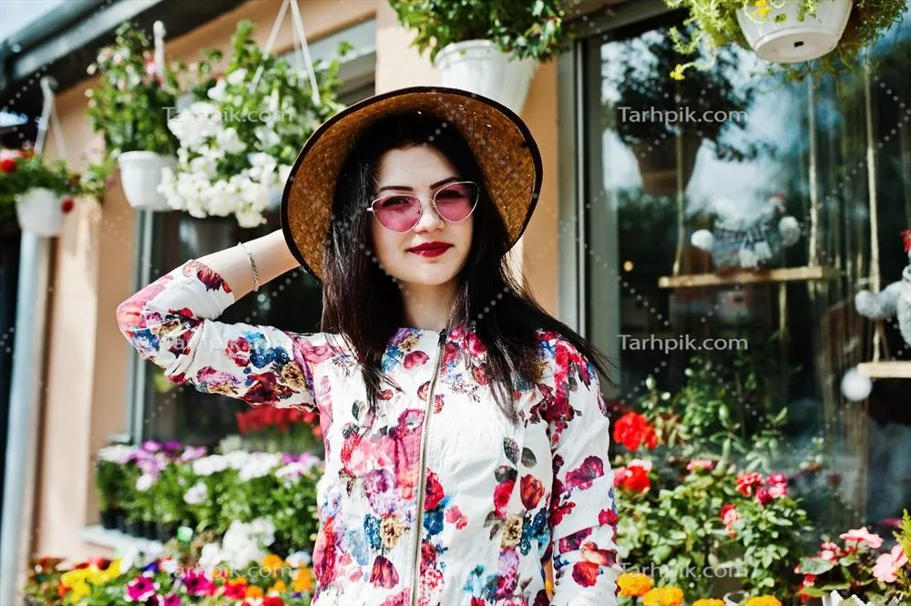 پرتره تابستانی دختر قهوه ای مو با عینک صورتی و کلاهی زیبا در برابر فروشگاه گل